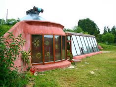 a house made out of clay and glass in the middle of a grassy area with trees around it