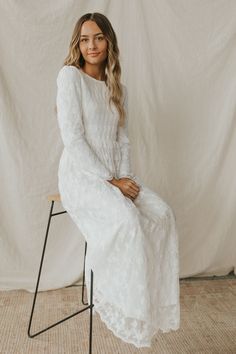 a woman sitting on a chair wearing a white dress with long sleeves and a lace skirt