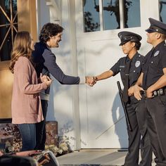 two police officers shaking hands in front of a door with a woman standing next to them