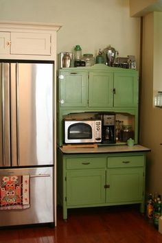 a kitchen with green cabinets and stainless steel refrigerator freezer combo in the corner, next to an old fashioned microwave oven