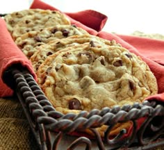 three chocolate chip cookies in a basket on a table top with red napkins next to it