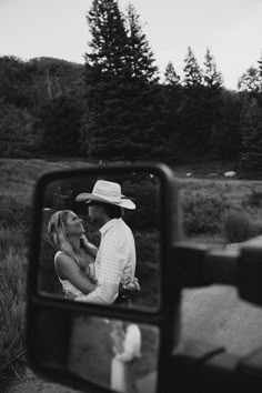 a black and white photo of a man kissing a woman in front of a car mirror