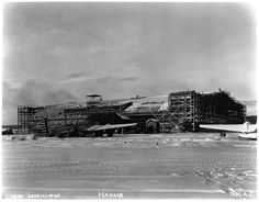 black and white photograph of an airplane being worked on in the snow with scaffolding around it