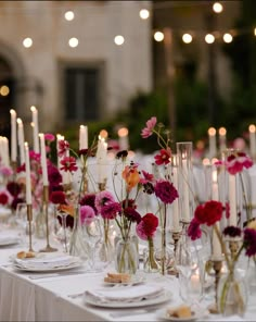 the table is set with candles and flowers in vases, plates and napkins