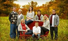 a group of people sitting on top of a red couch in the middle of a field