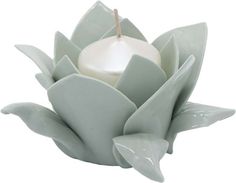 a white candle sitting on top of a green flower shaped vase with leaves around it