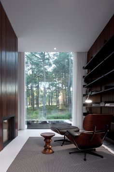 an empty room with a chair and ottoman in front of a large window that looks out onto the woods