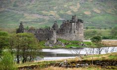 an old castle sitting on top of a lush green hillside next to a body of water