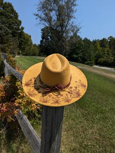 This tumeric yellow hand burnt wide brim fedora would make a perfect addition to any nature lover's wardrobe. The faux suede earthen yellow material burns a rich brown allowing the design to stand out. On the backside brim of the hat I hand burnt and shaded dandelion plants. On the front of the crown I burnt a single dandelion plant. I distressed the hat with stitch marks along the crown and brim of the hat. The design is original and completely free-handed. For a finishing touch I added a brown Handmade Yellow Wide Brim Straw Hat, Handmade Yellow Brimmed Hat, Yellow Bohemian Fedora Straw Hat, Yellow Bohemian Straw Hat With Curved Brim, Bohemian Yellow Straw Hat With Short Brim, Yellow Bohemian Straw Hat With Short Brim, Yellow Bohemian Wide Brim Straw Hat, Yellow Fedora Sun Hat For Kentucky Derby, Rustic Festival Hats For Spring