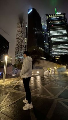 a man standing in the middle of a city at night with tall buildings behind him