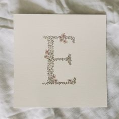 the letter e is made up of flowers and leaves on white paper with an embroidered edge