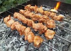 chicken skewers being cooked on a grill with coals in the foreground