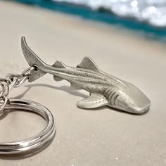 a metal shark keychain sitting on top of a sandy beach