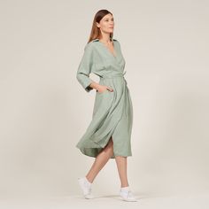 a woman in a green shirt dress is walking and looking off to the side with her hands on her hips