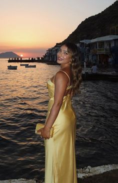 a woman in a yellow dress standing by the water