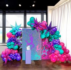 the balloon arch is decorated with pink, purple and green balloons in front of a large window