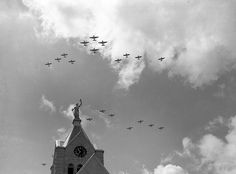 black and white photograph of airplanes flying in formation over a church steeple with clock