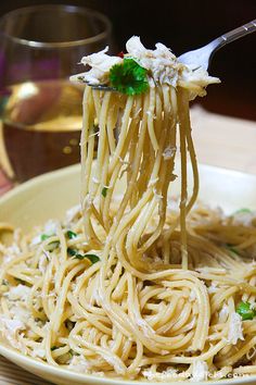 a fork full of noodles with chicken and parsley on top, in a bowl