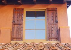 a window with wooden shutters on the side of a brown building next to a tiled roof