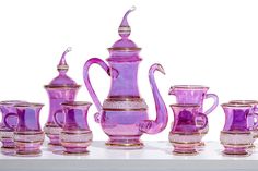 a collection of purple glass vases and cups on a white surface with gold trimming