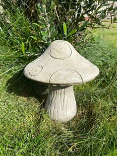 a stone mushroom sitting in the grass next to a bush