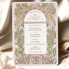 a wedding card with an ornate design on the front and back, sitting next to some flowers