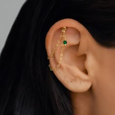 a woman wearing a gold chain ear cuff with a green stone