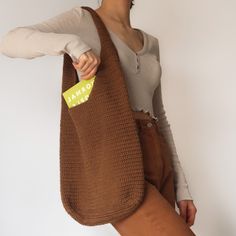 a woman holding a brown bag with a yellow tag on it's side and her right hand in the pocket