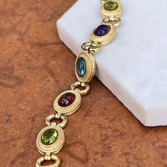 Estate/ vintage 14KT yellow gold Byzantine design, textured + cabochon, multi-gemstone link bracelet. Textured, shiny, and matte finishes on this piece. Slightly concave pieces with cabochon, amethyst, blue topaz, garnet, peridot, and citrine oval gemstones. Each gemstone measures: 7mm x 5mm; (8) total Rectangle byzantine + shiny open design links bracelet Measures 7.5", but fits shorter when clasped at the shorter length Weight: 22 grams Measures: 10mm wide Secure snap clasp Stamped 14K Great v Gold Oval Bracelet With Gemstone Accents, Oval Gold Bracelet With Gemstone Accents, Gold Oval Bracelets With Gemstone Accents, Oval Gold Bracelets With Gemstone Accents, Oval Gold Gemstones With Accents, Gold Jewelry With Gemstone Accents In Oval Cabochon, Gold Jewelry With Gemstone Accents And Oval Cabochon, Gold Jewelry With Gemstone Accents, Gold Multi-stone Oval Cabochon Jewelry