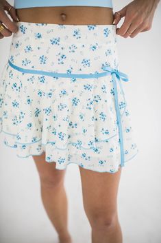 Our Desi mini skirt is the perfect summer skirt. We love the little bow detail and the blue flowers. The fabric is soft and flowy and perfect for summer days. You can even pair this skirt with a sweater and wear it into fall. How we would style it: Playful Daytime Look: Pair it with a blue tank and flip flops for a casual girly outfit. Evening Sophistication: Wear it with a tucked in blouse and ankle boots for a chic night out. Boho Vibes: Team it with a cropped knit sweater and cowboy boots for Summer Mini Skirt For Garden Party, Feminine Mini Hem Skirt For Summer, Summer Garden Party Mini Skirt, Summer Floral Print Mini Skirt For Day Out, Spring Beach Flared Skort, Spring Vacation Skirted Skort, Spring Daywear Skort With Relaxed Fit, Spring Mini Skirt For Daywear, Spring Daywear Mini Skirt