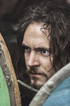 a close up of a person with long hair holding a shield and looking at the camera