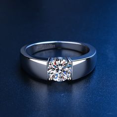 a white gold ring with a round brilliant cut diamond in the center on a blue surface