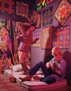 two people sitting on a bed in front of colorful paintings