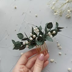 a person is holding a hair comb with flowers and leaves on it in their hand