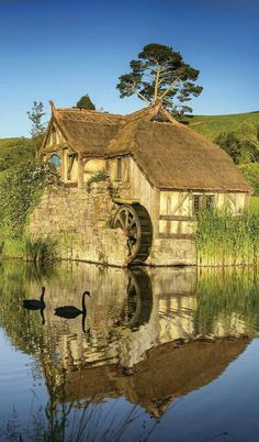 an old building with a water wheel in front of it on the side of a lake