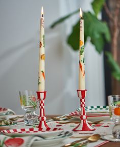 two candles sitting on top of a table next to plates and cups with utensils