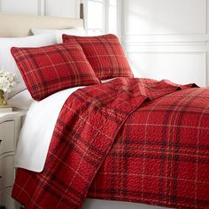 a bed with red and white plaid comforter in a bedroom next to a window