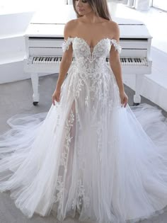 a woman standing in front of a piano wearing a wedding dress with sheer, off the shoulder sleeves