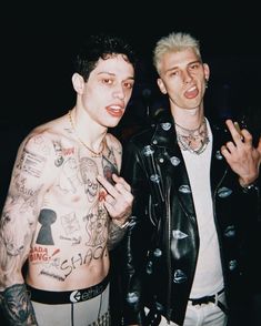 two men standing next to each other with tattoos on their arms and chest, posing for the camera