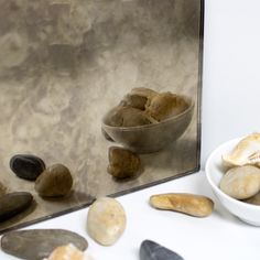 some rocks are sitting in front of a mirror and on the table there is a bowl of them