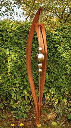 a metal sculpture with three balls on it in front of a hedge and shrubbery