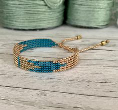 the blue and gold beaded bracelet is sitting on a wooden table next to spools of thread