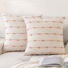 two pillows sitting on top of a white couch next to an open book in front of them