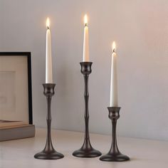 three candles are sitting on a table next to an open book and a framed photograph