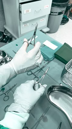 a person in white gloves holding scissors and other medical equipment on a table with silverware