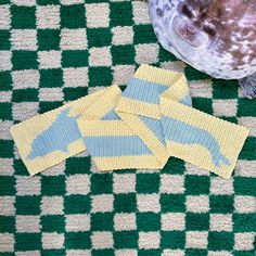 a sea lion laying on top of a green and white checkered rug next to two pieces of knitted cloth