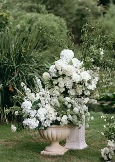 white flowers are in a large urn on the grass