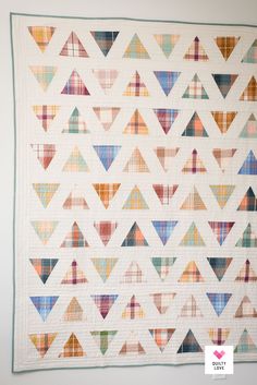 a quilted wall hanging on the side of a white wall with colorful triangles in it