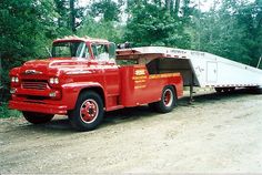 an old red truck with a trailer attached to it's bed is parked on the side of a dirt road