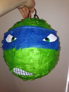 a hand holding a green and blue paper ball with eyes on it's face